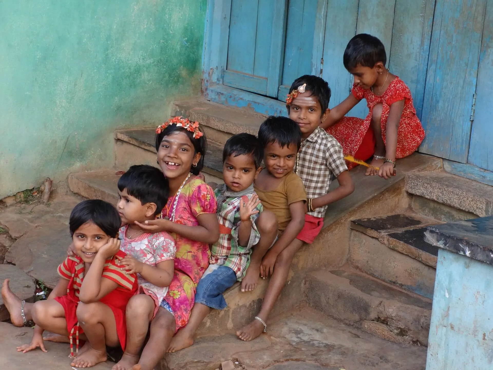 Children sitting together on the steps of a house with a bright blue door.