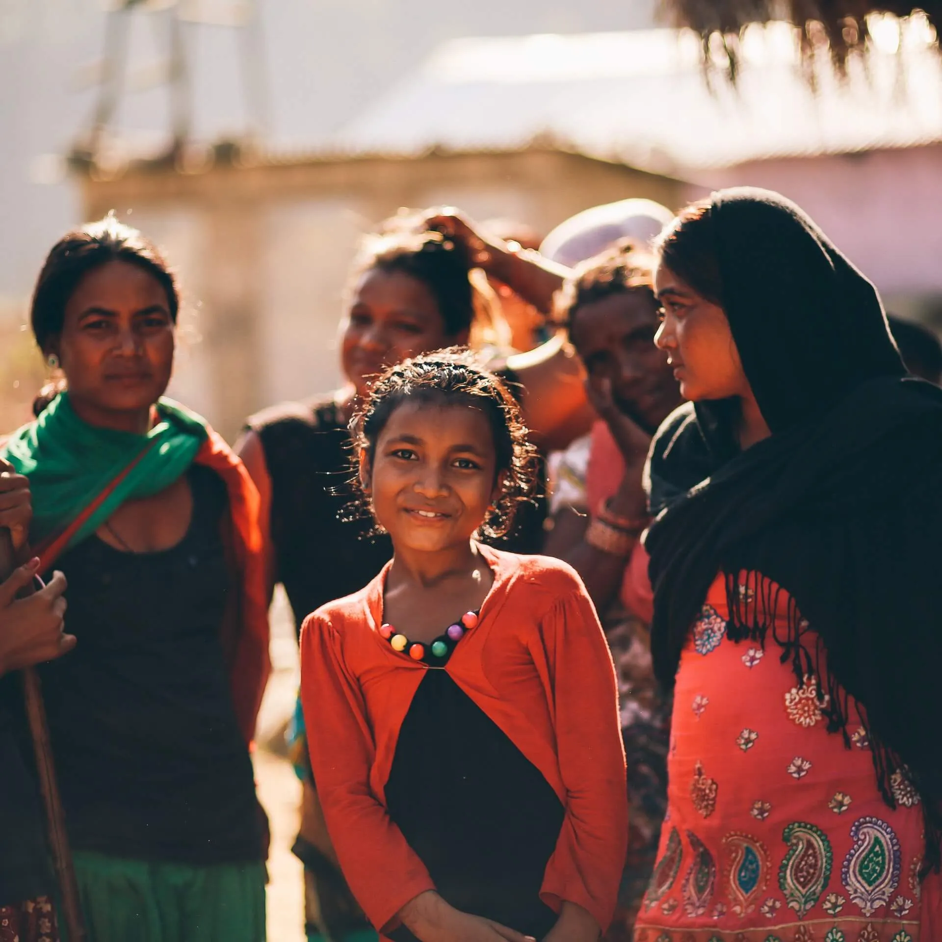 A girl smiling among women and children in a rural Indian community at golden hour.
