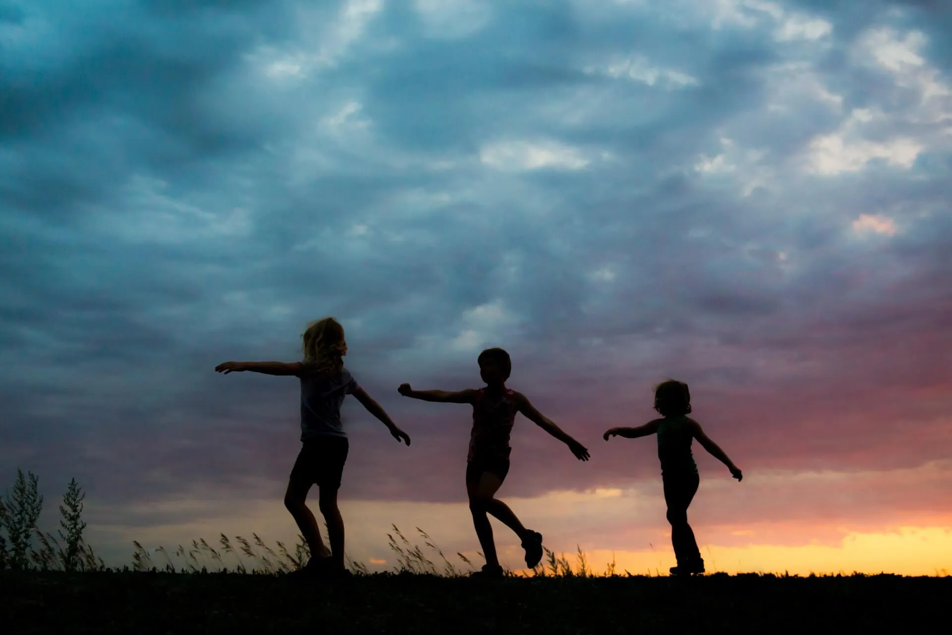 Three children playing outdoors, silhouetted against a sunset sky.
