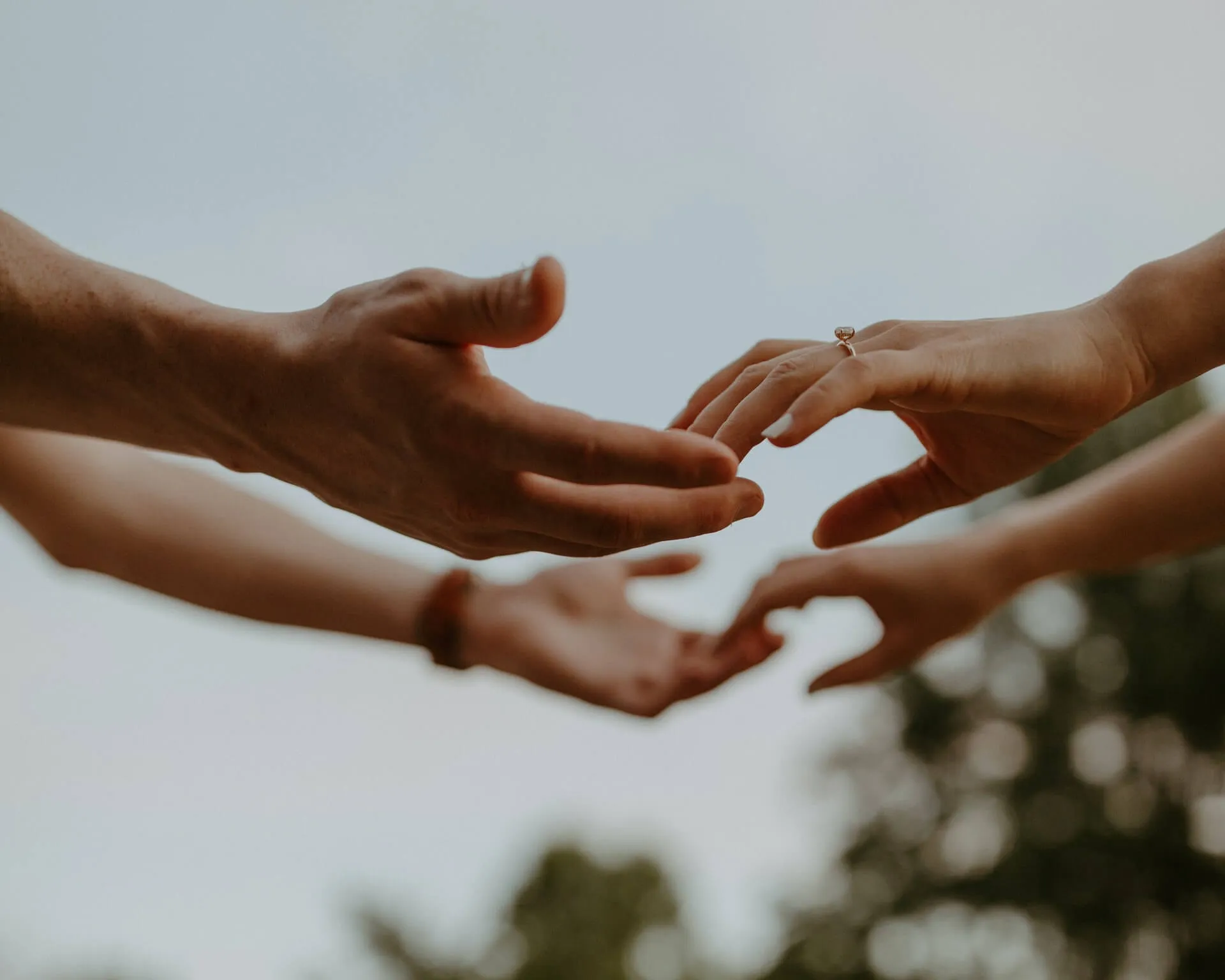 Two pairs of hands reaching toward each other against a pale sky.